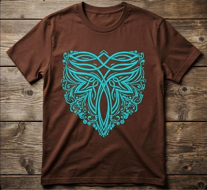 May include: A brown t-shirt featuring a teal, symmetrical design. The design is an intricate pattern of curved lines and floral elements, centered on the shirt's front. The shirt is displayed on a wooden surface.