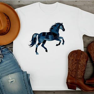 May include: White t-shirt with a denim patchwork horse graphic, paired with blue jeans, a brown cowboy hat, and brown leather cowboy boots. The items are arranged on a wooden surface, creating a rustic, Western-themed aesthetic.