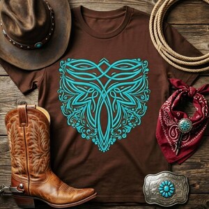 May include: A brown t-shirt with a turquoise floral design, cowboy boots, a cowboy hat, a red bandana, a silver belt buckle with turquoise accents, and a rope on a wooden surface. Western-themed apparel.