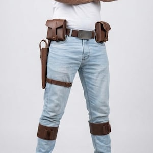 Puede incluir: Cintur&oacute;n utilitario de cuero marr&oacute;n con dos bolsillos, una funda y correas para las piernas. El cintur&oacute;n tiene una hebilla plateada y se usa con vaqueros azul claro y una camiseta blanca. Los accesorios de cuero son de color marr&oacute;n oscuro.