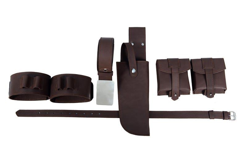 Puede incluir: Un conjunto de cintur&oacute;n utilitario de cuero marr&oacute;n, que incluye un cintur&oacute;n, dos portacartuchos, dos bolsas y una funda para cuchillos. El cintur&oacute;n tiene una hebilla plateada, sobre fondo blanco.