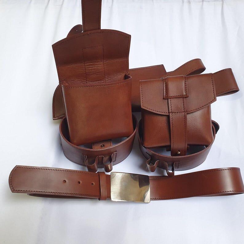 Puede incluir: Un cintur&oacute;n de cuero marr&oacute;n con hebilla plateada, acompa&ntilde;ado de dos bolsas a juego y una m&aacute;s grande, todas unidas al cintur&oacute;n. Las bolsas tienen forma rectangular con cierre de solapa. El cuero tiene una textura suave.
