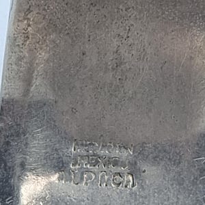Może przedstawiać: Zbliżenie srebrnego metalowego przedmiotu z tekstem "MEXICO" i "LPICH" wytłoczonym w metalu. Metal ma teksturowaną powierzchnię z pewnymi śladami zużycia.