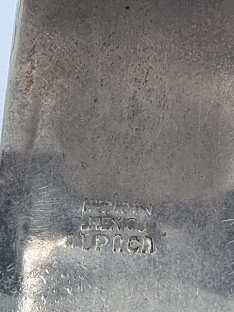 Może przedstawiać: Zbliżenie srebrnego metalowego przedmiotu z tekstem "MEXICO" i "LPICH" wytłoczonym w metalu. Metal ma teksturowaną powierzchnię z pewnymi śladami zużycia.