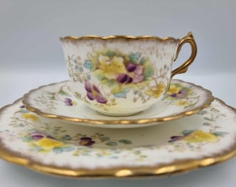 Puede incluir: Juego de té vintage de porcelana blanca con diseño floral en amarillo y morado y ribete dorado. El juego incluye taza, platillo y plato. La taza tiene asa dorada y borde festoneado. Ideal para la hora del té.