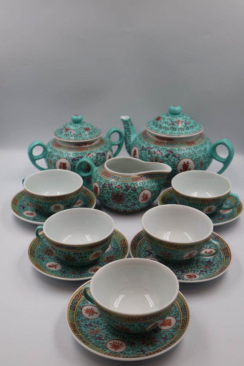 Puede incluir: Juego de t&eacute; turquesa con un patr&oacute;n floral y geom&eacute;trico. El juego incluye dos teteras, una lechera, seis tazas y platillos. El juego de t&eacute; tiene un dise&ntilde;o asi&aacute;tico tradicional con detalles en rojo y dorado.