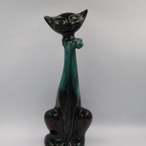 Może przedstawiać: Wysoka, ceramiczna figurka kota o smukłym, wydłużonym kształcie. Kot ma czarną głowę i tułów z turkusowo-zieloną szyją i muszką. Błyszczące wykończenie dodaje elegancji temu elementowi dekoracyjnemu.