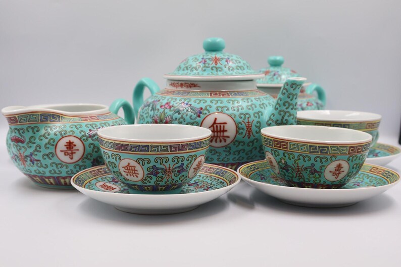 Puede incluir: Un juego de t&eacute; turquesa completo con tetera, crema, tazas y platillos. El juego presenta un estampado floral con caracteres chinos rojos. La tetera tiene forma redondeada con tapa y asa. Las tazas y platillos son peque&ntilde;os y delicados.