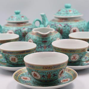 Puede incluir: Juego de t&eacute; turquesa con dise&ntilde;os florales y geom&eacute;tricos. El juego incluye una tetera, una jarra de crema, tazas y platillos. Cada pieza presenta un borde dorado y caracteres chinos.