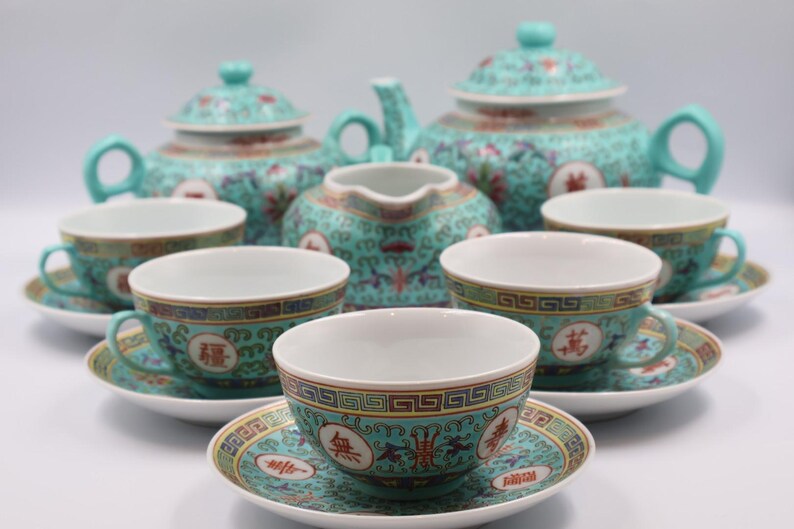 Puede incluir: Juego de t&eacute; turquesa con dise&ntilde;os florales y geom&eacute;tricos. El juego incluye una tetera, una jarra de crema, tazas y platillos. Cada pieza presenta un borde dorado y caracteres chinos.