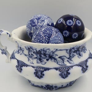 Może przedstawiać: Biało-niebieska porcelanowa miska z uchwytem, wypełniona trzema dekoracyjnymi kulami z niebiesko-białym wzorem. Miska ma niebieski kwiatowy wzór. Kule mają różne wzory.