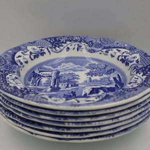 Puede incluir: Una pila de seis platos de cerámica azules y blancos. Cada plato presenta una escena de paisaje detallada en el centro, rodeada por un borde floral y de volutas. Los platos están apilados ordenadamente, mostrando su diseño clásico.