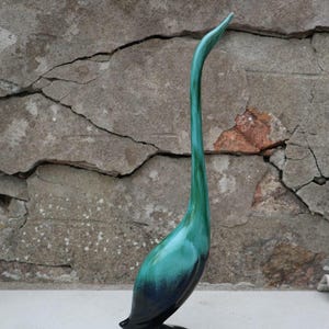 May include: A tall, slender bird figurine featuring a smooth, glossy finish with a gradient color scheme that transitions from a deep, dark navy blue at the base to a vibrant, bright teal green along the elongated neck and pointed beak.