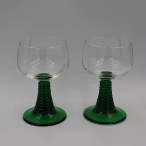 May include: A white ceramic mug with a black handle and the text "But First, Coffee" in a black, bold font. The mug is on a wooden surface. The mug is 10 cm tall.