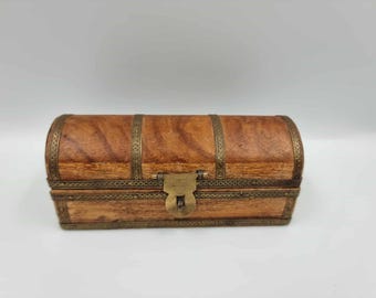 May include: A small, rectangular wooden chest with a curved top. The chest is made of light brown wood and is accented with brass-colored metal trim and a clasp. The chest is likely used for storing small items.