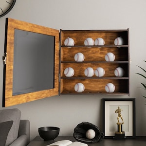 May include: A wooden baseball display case with a glass door, featuring 10 baseballs on shelves. The case is mounted on a wall and has a dark brown finish.