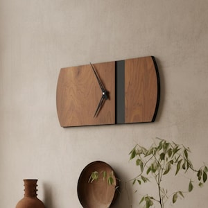 May include: A rectangular wooden wall clock with a dark grey vertical stripe and black hands. The clock is mounted on a light beige wall. The clock's dimensions are approximately 61 cm long and 30 cm wide. The clock is part of a kitchen decor.
