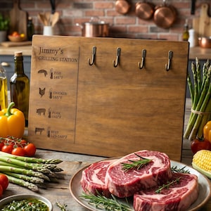 Könnte beinhalten: Ein hölzernes Grillstationsschild mit Haken, mit dem Text "Jimmy's GRILLING STATION" und Kochtemperaturen für Fisch, Huhn, Schweinefleisch und Rindfleisch. Das Bild enthält auch rohe Steaks, Gemüse und Kräuter.