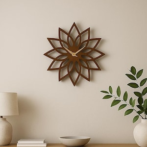 Könnte beinhalten: Eine braune Wanduhr aus Holz in Blumenform mit goldenen Zeigern. Die Uhr ist an einer beigefarbenen Wand über einem Holzschrank angebracht. Eine Lampe, Bücher und eine dekorative Schale befinden sich auf dem Schrank.