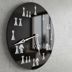 May include: A black round wall clock with white chess piece hour markers. The clock hands are white and black. The clock is mounted on a white brick wall.