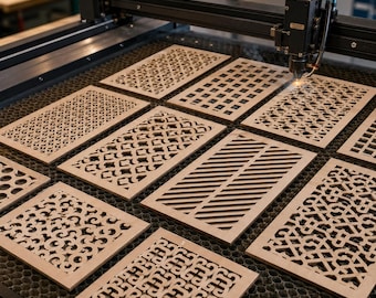May include: A laser cutting machine with a black metal gantry and a focused laser head is actively engraving or cutting a series of rectangular light-coloured wooden panels featuring various intricate geometric and lattice patterns on a honeycomb bed.