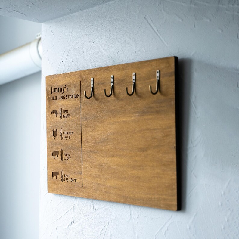 May include: A wooden grilling station with hooks and a chart listing recommended internal temperatures for different types of meat, including fish, chicken, pork, and beef. The chart is labeled "Jimmy's Grilling Station".