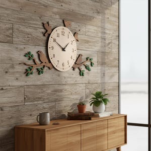 May include: A wooden wall clock with a light-colored face and black hands. The clock features a bird and branch design, with birds perched on branches with green leaves. The clock is mounted on a wooden wall.