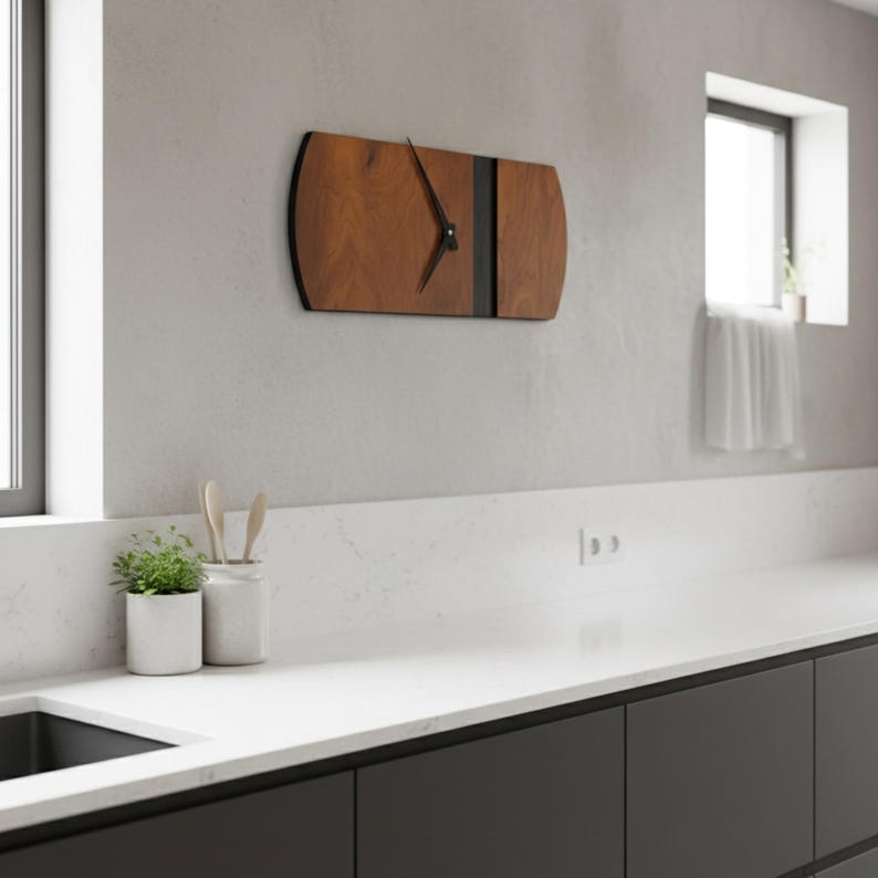 May include: A rectangular wooden wall clock with a dark brown finish and black accents. The clock has a minimalist design with black clock hands. The clock is mounted on a light gray wall in a kitchen setting.