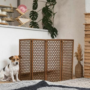 May include: A brown wooden room divider with a circular pattern. The divider is made of four panels and is standing on a white rug. A small white and brown dog is sitting in front of the divider.