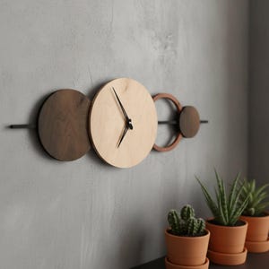 May include: A modern wall clock with a minimalist design. The clock features a light wood face with black hands, a dark wood circle, and a copper-colored ring. The clock is mounted on a gray wall.