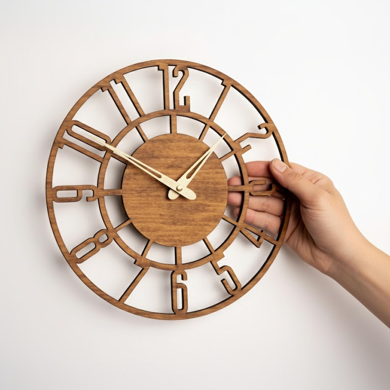 Puede incluir: Un reloj de madera redondo con acabado marr&oacute;n claro. El reloj presenta n&uacute;meros romanos y un dise&ntilde;o circular. Las manecillas son de color crema claro. Una persona sostiene el reloj.