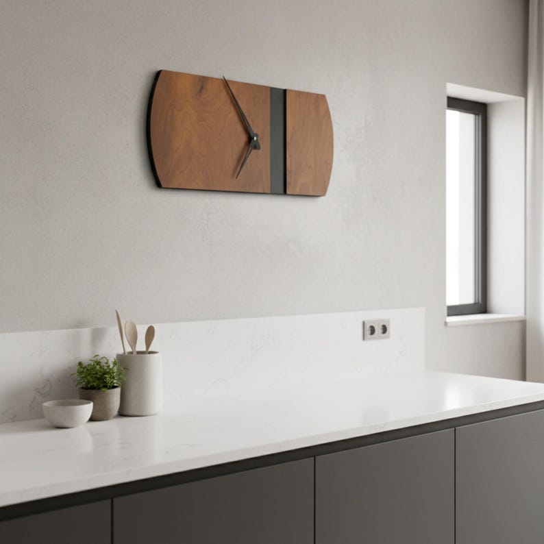 May include: A modern wooden wall clock with a dark gray stripe and black hands. The clock is mounted on a light gray wall. The clock's face is a light brown color. The clock is rectangular with rounded edges.