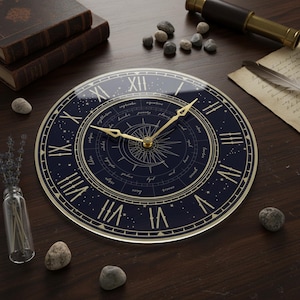 Puede incluir: Un reloj de pared redondo con esfera azul marino y números romanos dorados. El reloj tiene manecillas doradas y un diseño de brújula en el centro. Elementos decorativos como libros y piedras rodean el reloj.