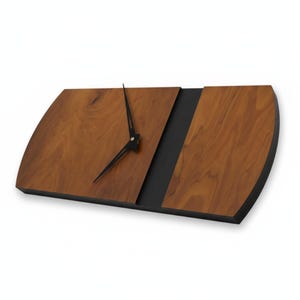 May include: A modern wooden clock with a unique design. The clock features a light brown wooden face with a black stripe down the middle and black clock hands. The clock is approximately 15 inches long.