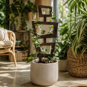 Op de afbeelding: Een donkerbruin houten plantenrek met een geometrisch, gestapeld rechthoekig ontwerp, dat een groene klimop ondersteunt die groeit in een ronde, crèmekleurige keramische pot met verticale geribbelde texturen aan de buitenkant.