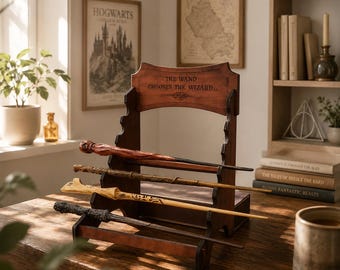 Puede incluir: Un expositor de varitas de madera con cuatro varitas. El expositor tiene el texto "THE WAND CHOOSES THE WIZARD." Las varitas son de varios colores y diseños. La exhibición está sobre una mesa de madera.