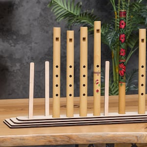 May include: A wooden stand with eight slots holds a collection of wooden flutes. The flutes are natural wood colour with some painted with red and white floral designs.