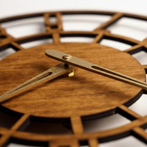Puede incluir: Primer plano de un reloj de madera con esfera marr&oacute;n oscuro y marco negro. Las manecillas del reloj son doradas. El reloj tiene un dise&ntilde;o decorativo y abierto con n&uacute;meros romanos.