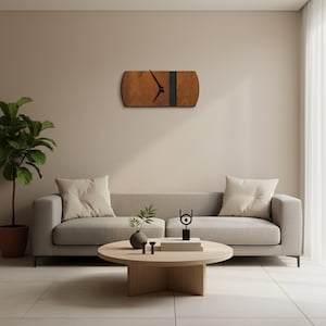 May include: A rectangular wooden wall clock with a dark vertical stripe and black clock hands. The clock is mounted on a beige wall above a gray sofa. The room has a neutral color palette with a plant and a round coffee table.