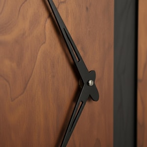 May include: Close-up of a modern wall clock with a dark wood grain face and black hands. The clock hands are thin and elegant, with a minimalist design. The clock face has a natural wood finish.