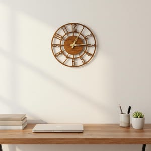 Puede incluir: Un reloj redondo de madera con n&uacute;meros romanos y un acabado marr&oacute;n claro. El reloj est&aacute; montado en una pared blanca. Las manecillas del reloj son de color dorado claro. El reloj tiene aproximadamente 30 cm de di&aacute;metro.
