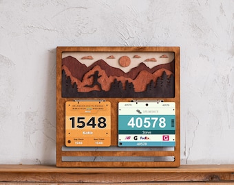May include: Wooden display frame with a mountain scene and two race bib holders. The frame features a runner silhouette, a sun, and the text "ERLANGER CHATTANOOGA MARATHON". Two race bibs are displayed with the numbers 1548 and 40578.