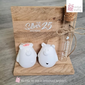 Könnte beinhalten: Eine hölzerne Hochzeitsdekoration mit dem Text "Zur Silber 25 Hochzeit". Sie zeigt zwei weiße Bärenfiguren, ein Reagenzglas mit Korken und den Text "Herzlichen Glückwunsch". Der Text "Mit Liebe Für Dich in Deutschland hergestellt" ist ebenfalls vorhanden.