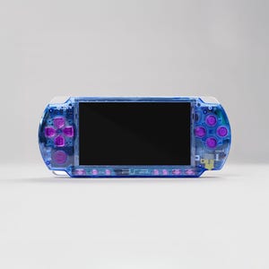 May include: A transparent blue handheld games console with purple buttons and a black screen. The console has the text "SONY" and "PSP" visible. The design features a clear plastic casing, showcasing the internal components.