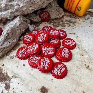 May include: A pile of red bottle caps with the words "Nuka Cola" printed in white. The caps are on a rusty metal surface.