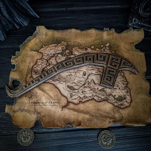 May include: A wooden map of the Province of Skyrim with a decorative weapon on top. The map is aged with a brown and tan color scheme. Two bronze coins are at the bottom. The weapon has a geometric design.