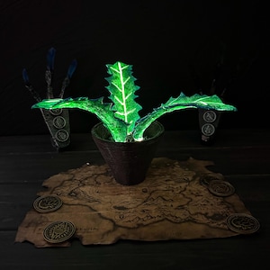 May include: A glowing green plant in a brown pot, set on a map with coins. The plant has spiky leaves with white veins. The pot sits on a detailed map with several bronze coins around it. The background is dark, with two stylized hand-like figures.
