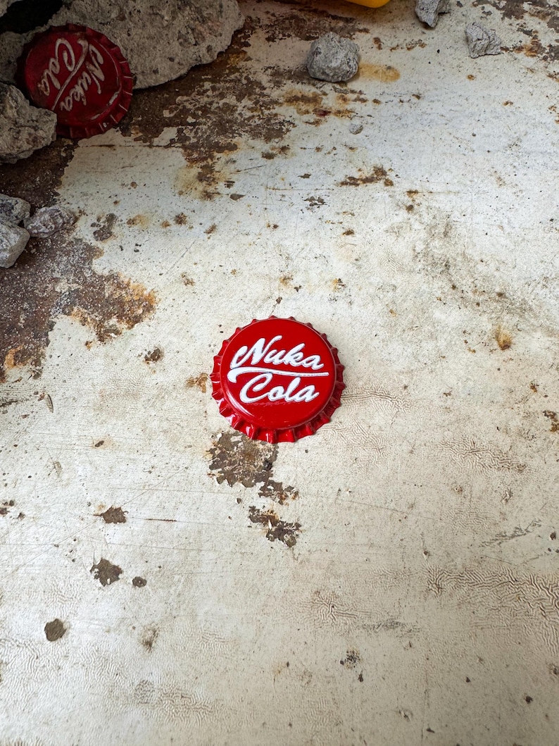 May include: Red bottle cap with white text that reads "Nuka Cola".