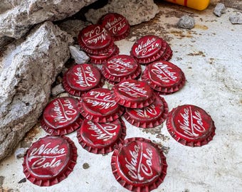 May include: A pile of red bottle caps with the words "Nuka Cola" printed on them. The bottle caps are scattered on a white surface with rust-colored stains.