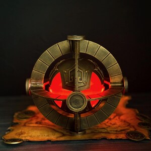 May include: A bronze-colored, spherical decorative object with a glowing red interior. The object has an intricate design with circular and geometric shapes. It sits on a map with coins, suggesting a fantasy or historical theme.